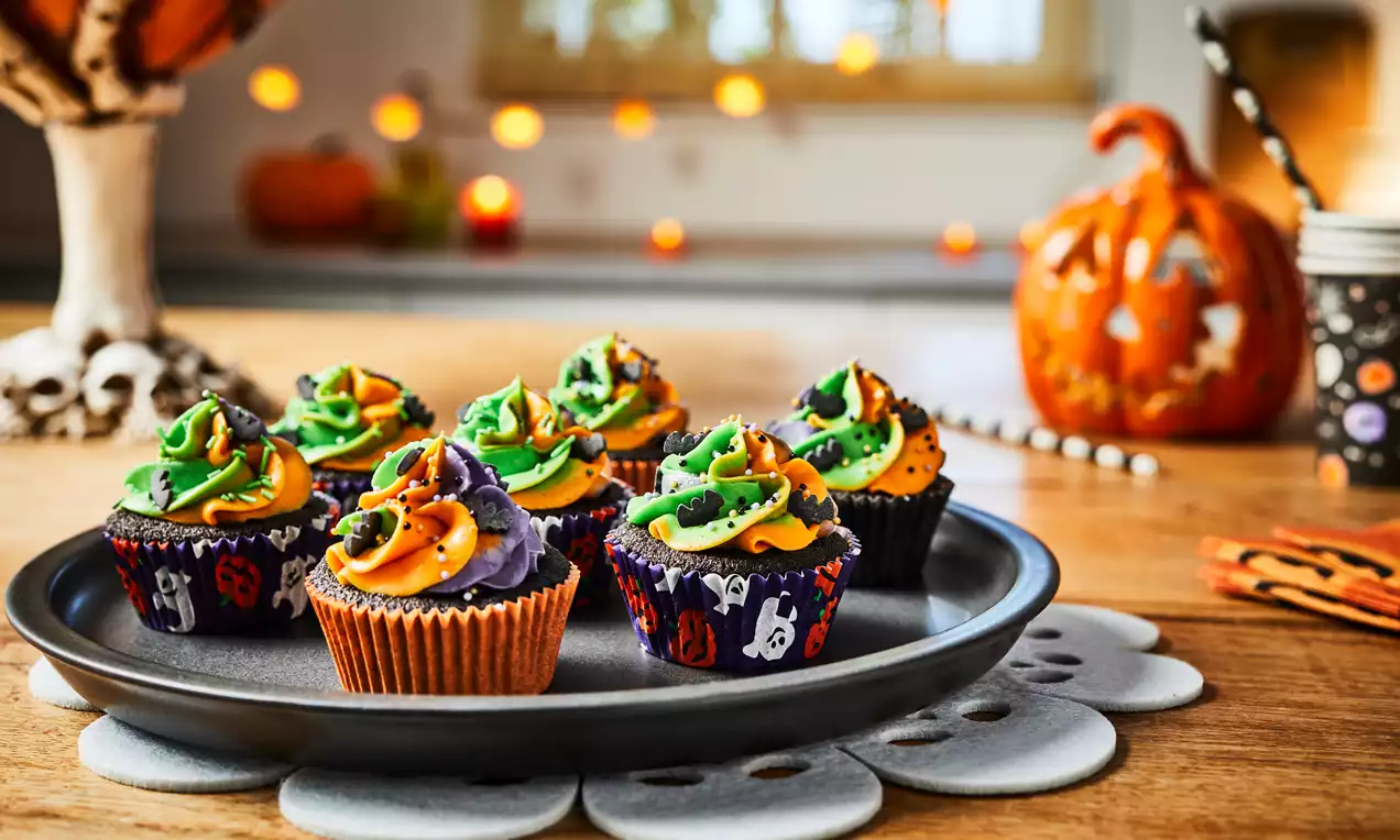 Halloween-cupcakes med swirl-toppe i orange, grøn og lilla glasur, pyntet med stjerner og drys, placeret på en sort tallerken