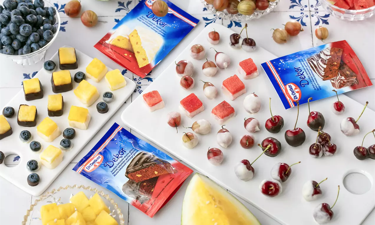 Ant baltų paviršių matomi spalvingi vaisių ir uogų gabalėliai – raudonos vyšnios, geltoni ananasai, mėlynos šilauogės, sultingos arbūzo skiltelės