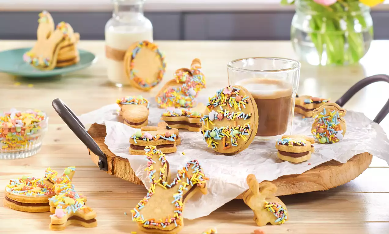 Gefüllte Osterkekse in Hasenform mit goldbrauner Kruste und dunkler Nougatfüllung, halbiert auf Teller und mit bunten Streuseln bestreut