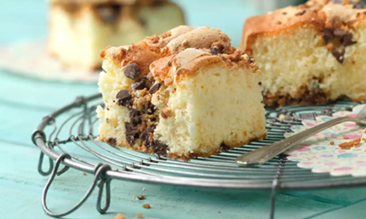 Cuadrados esponjosos de bizcocho dorado con trozos de chocolate y crocanti dispuestos en una rejilla sobre fondo turquesa