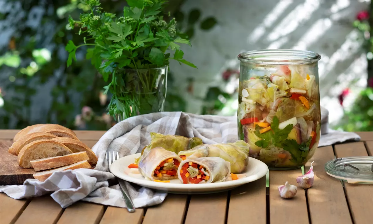 Завити сарми с леко прозрачни зелени листа, разкриващи разноцветни зеленчуци, подредени в бяла чиния върху дървена маса