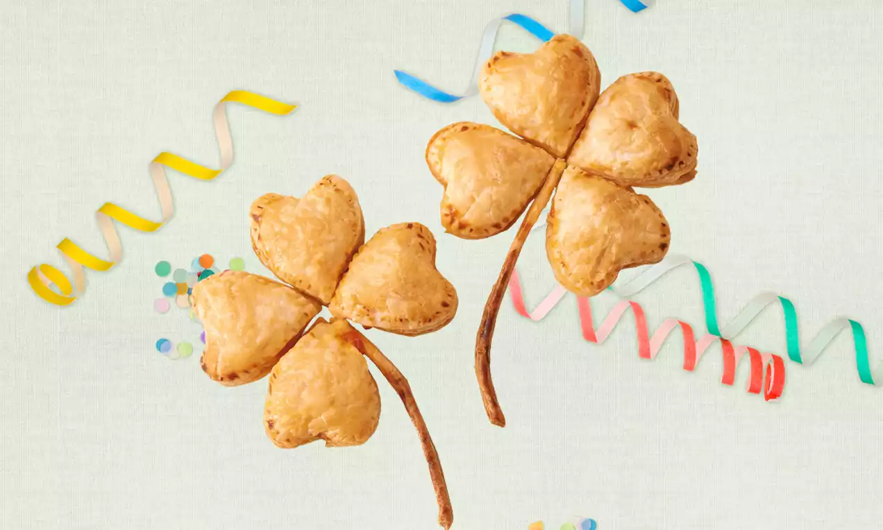 Aranybarnára sült, szív alakú tésztalevelek lóherére emlékeztető elrendezésben, vékony, ropogós szárakkal, színes szalagok és konfetti között