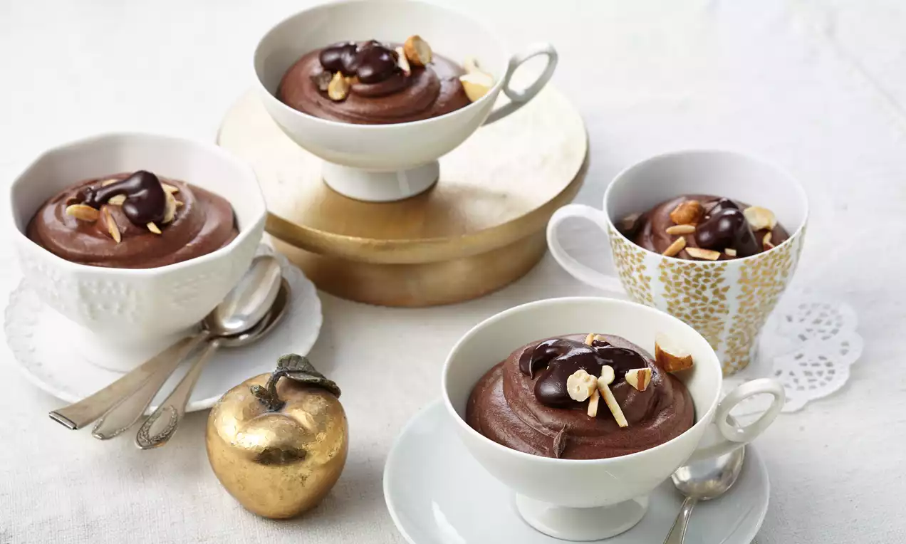 Zarte Schokoladencreme mit glatter Oberfläche, glänzender Ganache und gehackten Nüssen serviert in weißen und goldenen Tassen