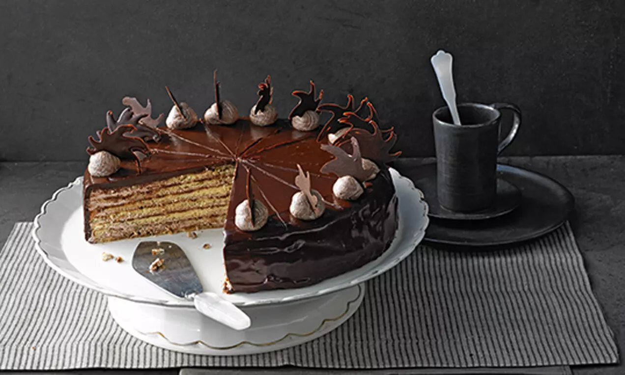 Торта с шоколадова глазура и пластове светло жълт пандишпан, украсена с шоколадови фигури и крем, поднесена на бяла чиния