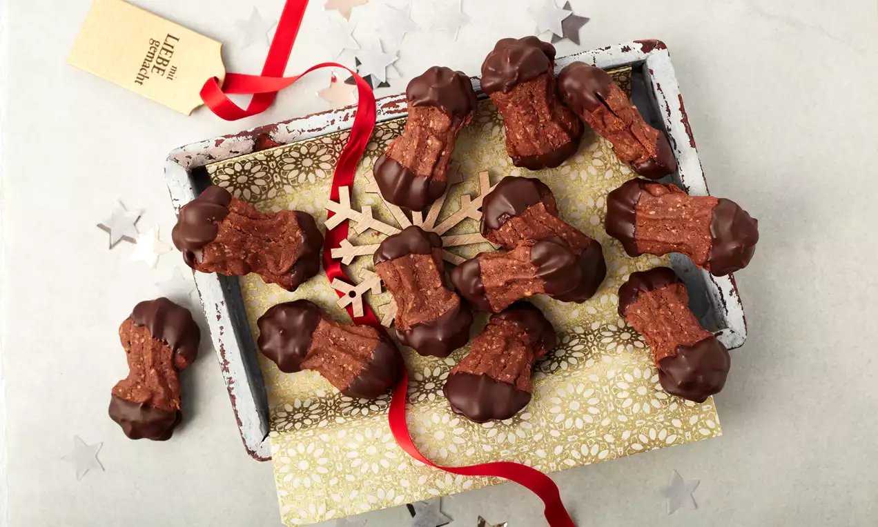 Nougatstangen mit dunkler Schokoladen-Umhüllung an den Enden auf weihnachtlichem Tablett mit Sternendekor und rotem Geschenkband