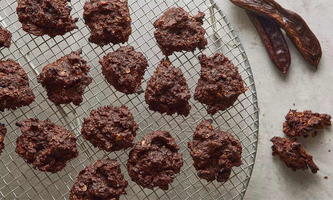 Tel ızgara üzerinde serili düzensiz şekilli keçiboynuzlu kurabiyeler koyu kahverengi ve pütürlü dokulu, yanlarında keçiboynuzu parçaları ile birlikte