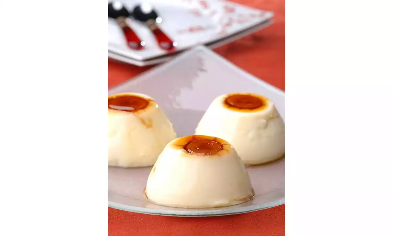 Beyaz cam tabakta sunulan, pürüzsüz ve parlak yüzeyli üç puding, üstlerinde akışkan karamel sosuyla ahenkli bir şekilde sıralanmış