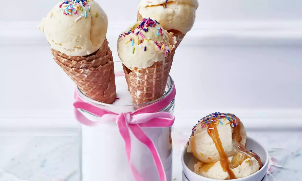 Fyra ljusgulvita vaniljglasskulor, tre i rån i glasburk med rosa band och en i vit skål, toppade med färgglatt strössel