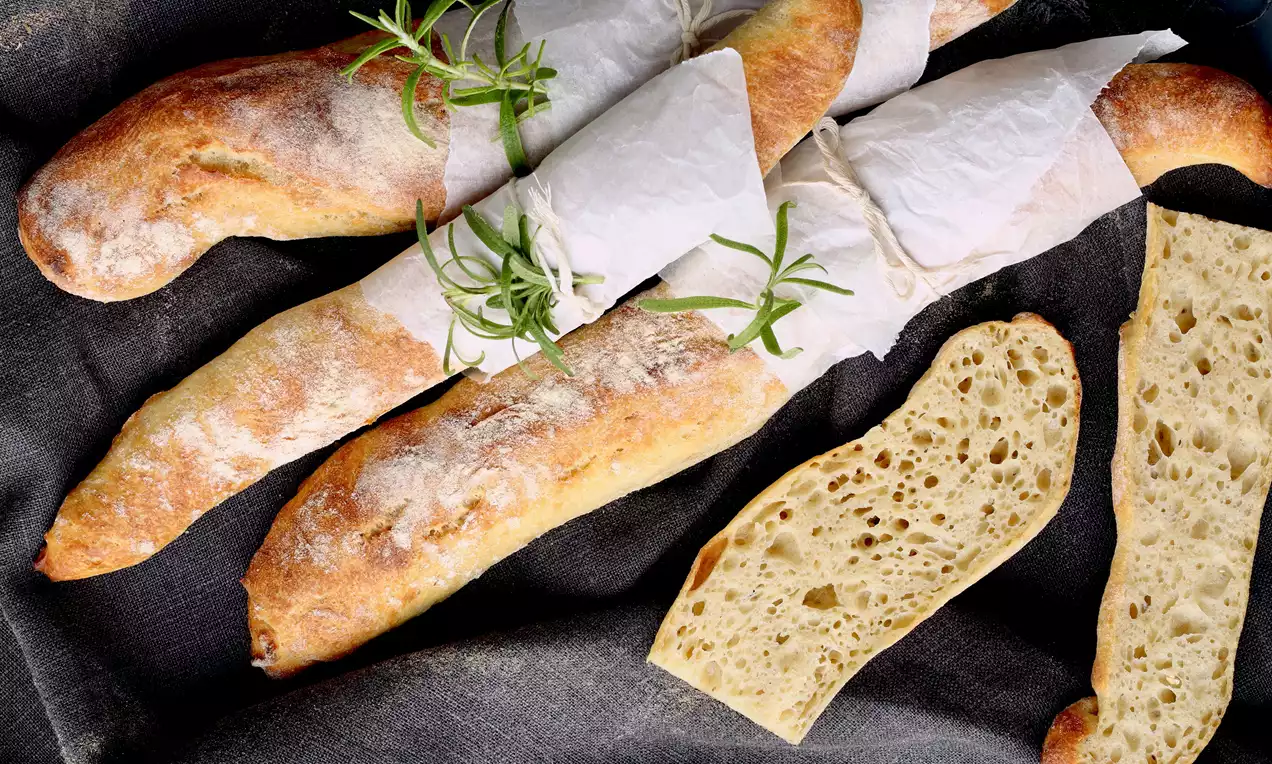 Pitkät ja kapeat, kullanruskeiksi paistetut leivät pehmeällä ja huokoisella sisuksella, rullattu vaaleaan paperiin ja koristeltu tuoreilla rosmariininoksilla