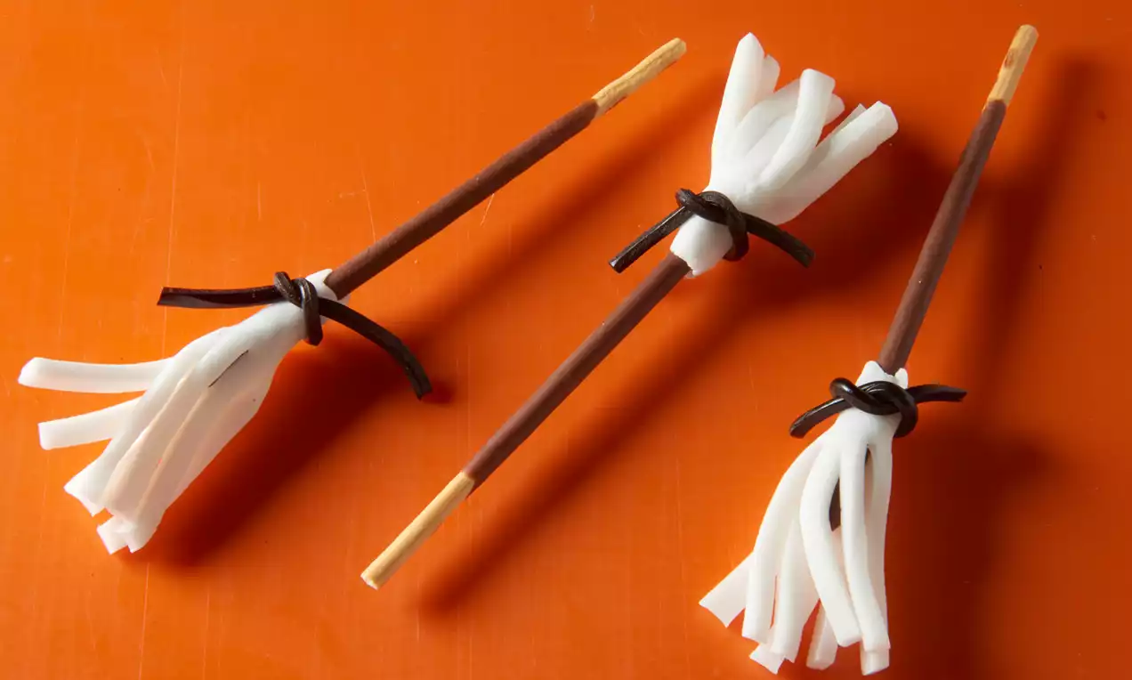 Petits balais en forme de baguettes brunes avec des franges blanches enroulées de cordons noirs sur un fond orange lumineux