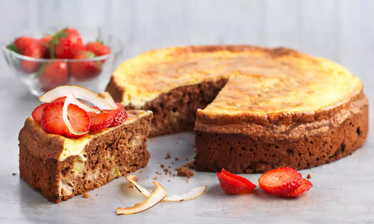 Rhabarber-Kokos-Kuchen mit golden gebackener Oberfläche, saftiger Textur und Erdbeerscheiben sowie Kokosspänen als Deko auf hellem Teller