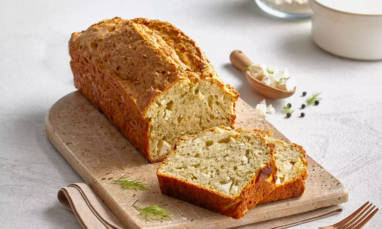 Altın kahverengi kabuğa sahip, içi dereotu ve beyaz peynir parçalarıyla dolu, dilimlenmiş dereotlu kek doğal taş üzerinde sunulmuş