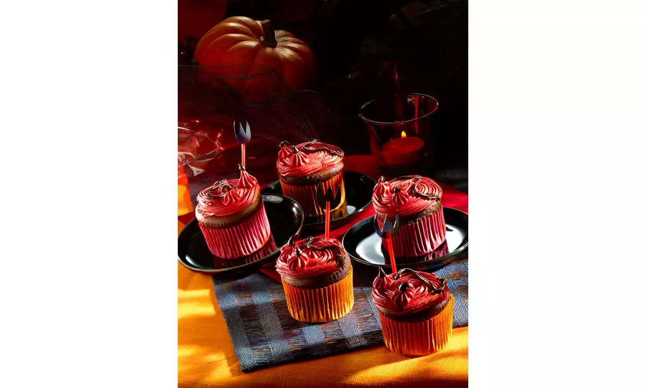 Cupcakes aux crèmes rouges tourbillonnantes surmontés de piques, présentés sur des assiettes noires avec un décor d'Halloween chaleureux