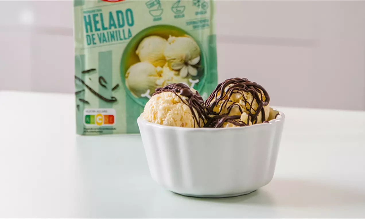 Bolas de helado amarillo pálido en un cuenco blanco con hilos de chocolate oscuro brillante y fondo de envase verde claro