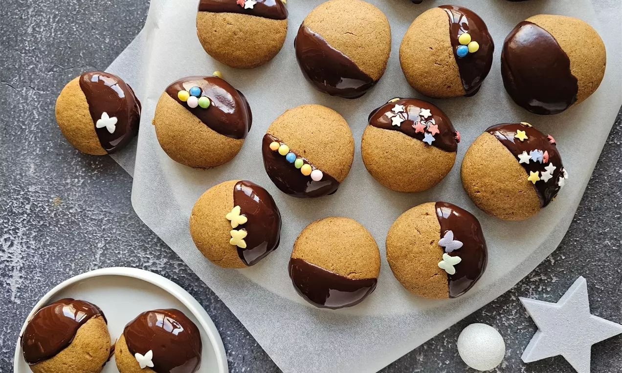 Кръгли меденки с мека текстура, покрити наполовина с лъскав шоколадов ганаш и цветни захарни декорации върху хартия и малка чиния