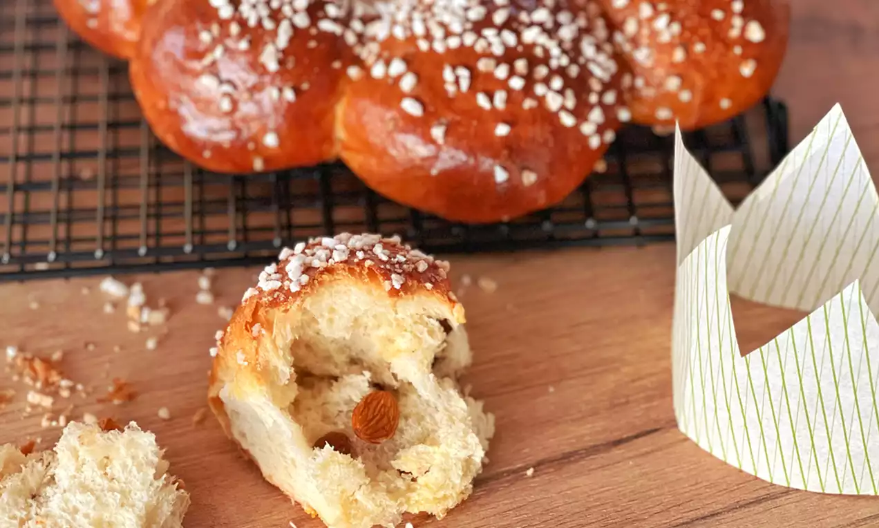 Goldbrauner Dreikönigskuchen in runder Form mit glänzender, bestreuter Kruste auf Gitterrost, daneben eine gold-weiße Papierkrone