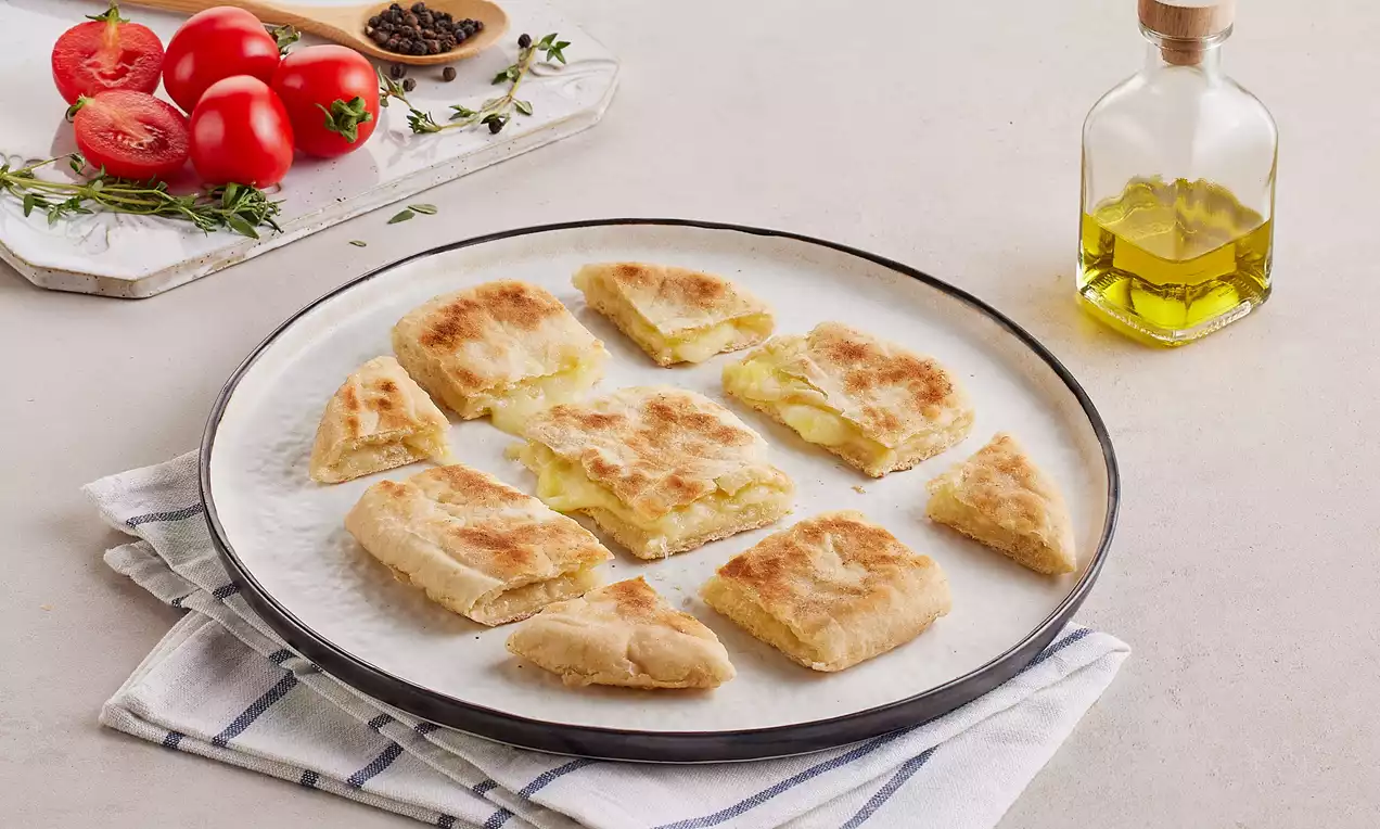 Altın renkli, hafif gevrek dokulu ve yumuşak iç dolgulu kare dilimler, beyaz tabakta desenli bez üzerinde düzenlenmiş