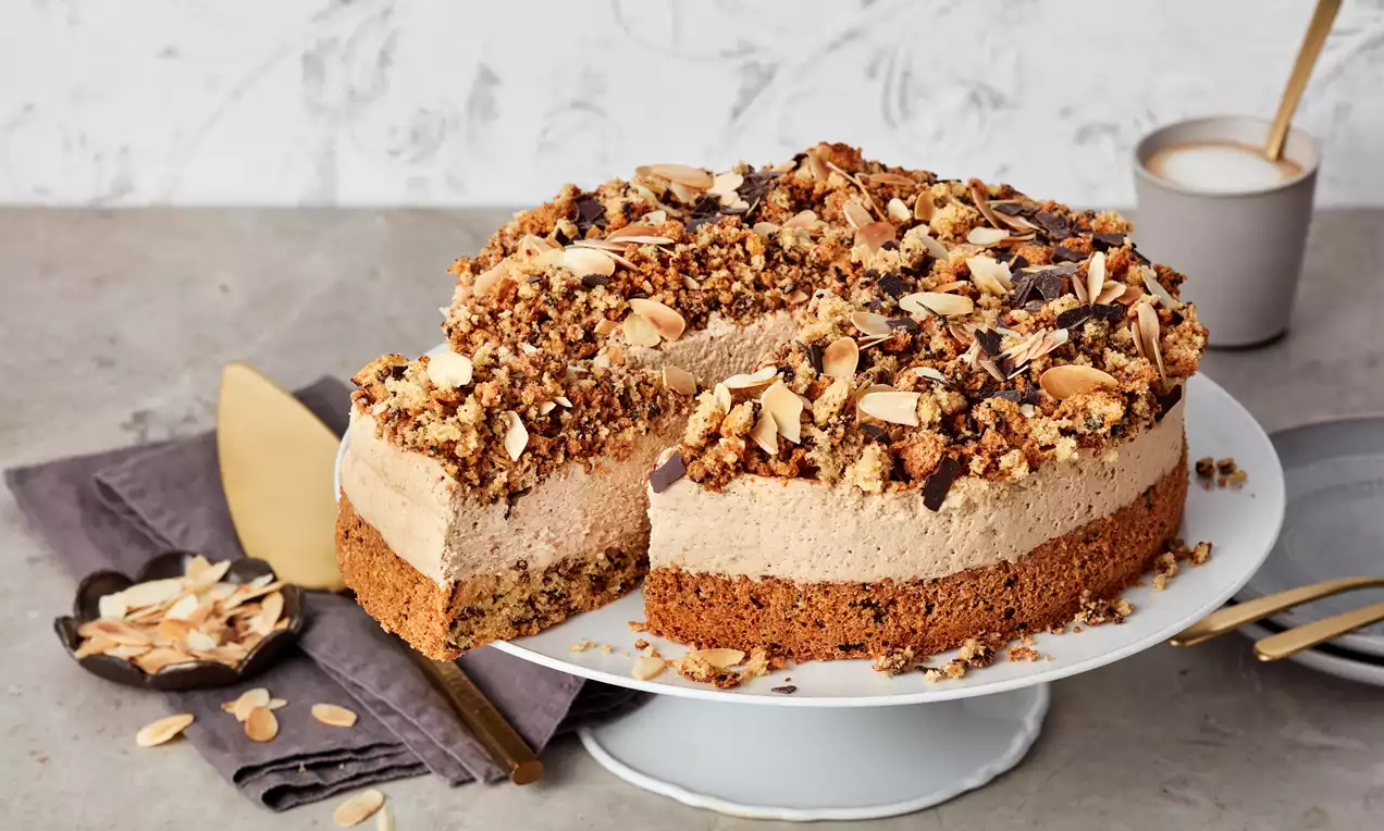 Eiskaffee-Torte mit lockerem Kaffeekern, heller Creme und knusprigem Mandel-Schokoladen-Topping auf weißer Tortenplatte angerichtet