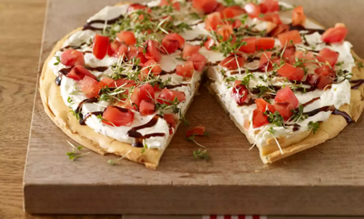 Herzhafte Torte mit glatter Frischkäsecreme auf goldbraunem Boden, belegt mit roten Tomatenwürfeln, Kresse und dunklem Balsamico