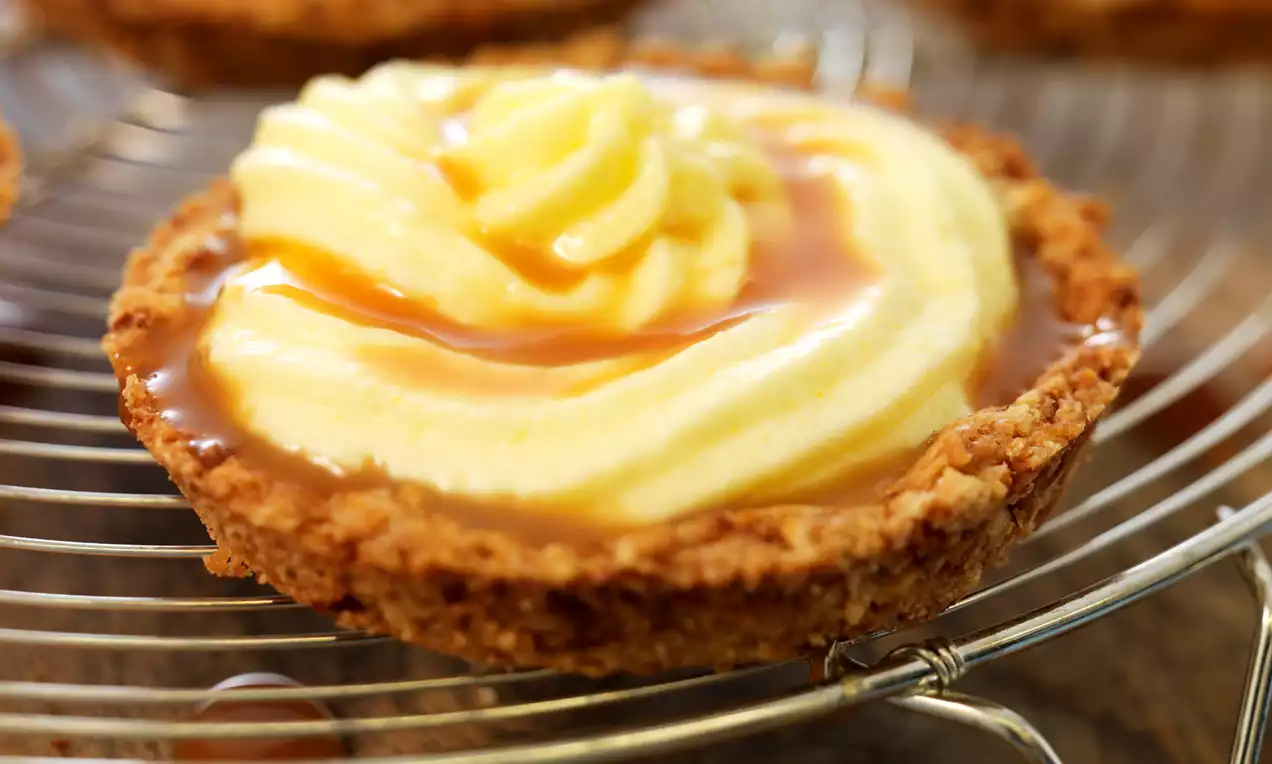Tartelettes met krokante, goudbruine randen gevuld met luchtige gele crème en gegarneerd met een dunne laag karamel op een metalen rooster