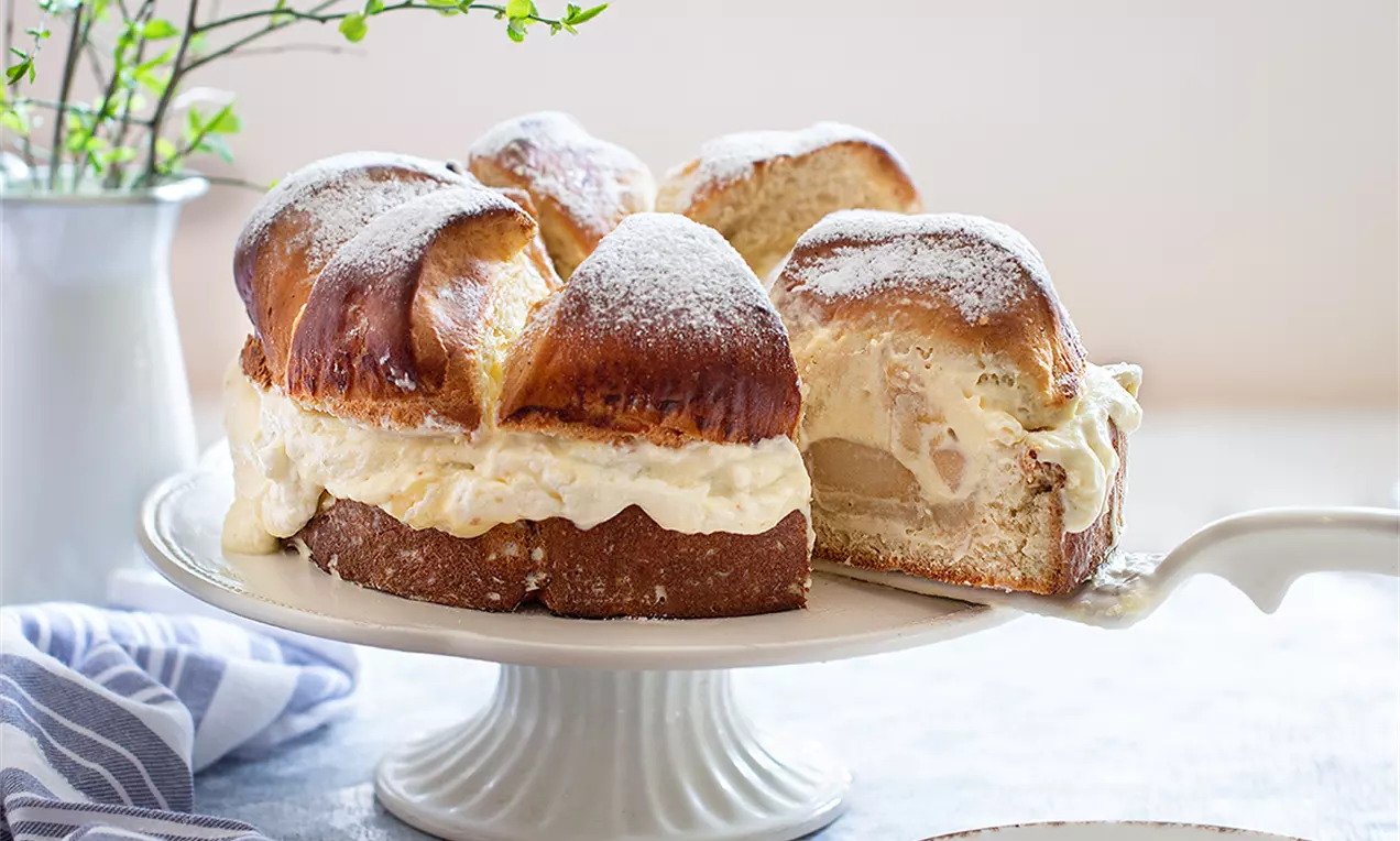 Шведска пита с пухкави златистокафяви слоеве, бяла кремообразна плънка и поръсена пудра захар върху порцеланова стойка