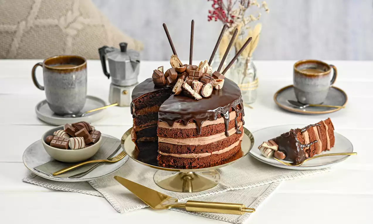 Gâteau au chocolat en couches riches, glaçage brillant, garni de biscuits et bâtonnets chocolatés, présenté sur un plat doré avec une tranche servie