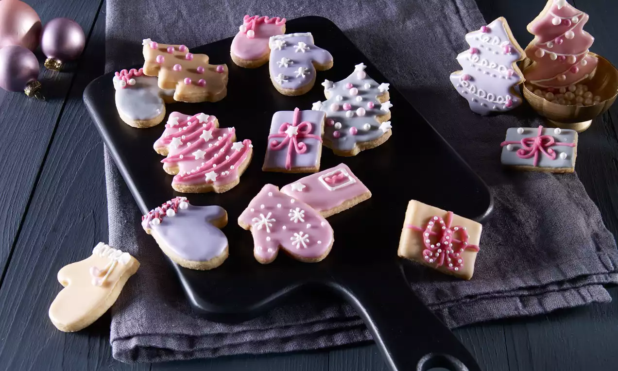 Zitronenplätzchen in weihnachtlichen Formen mit feiner Glasur und Dekor aus Perlen und Zuckerguss auf dunklem Brett mit Deko-Elementen drapiert