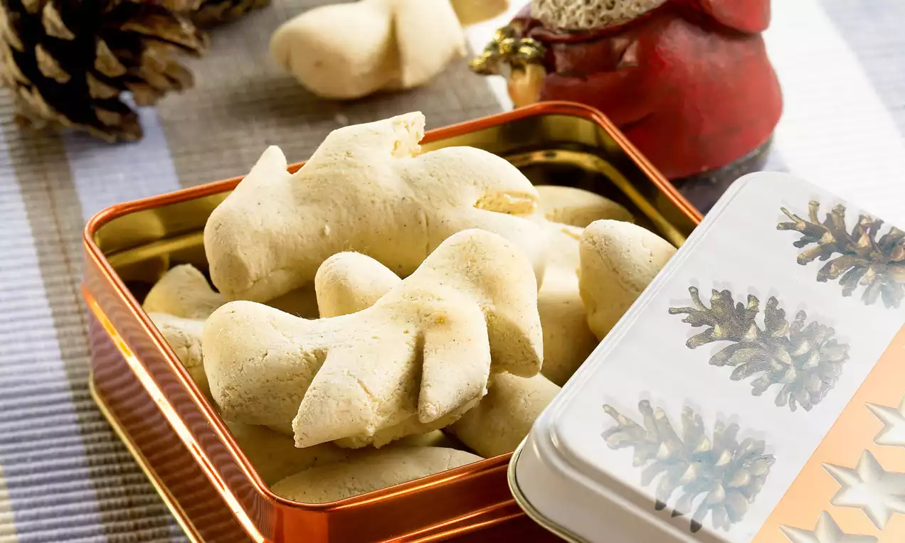 Petits biscuits croquants beige clair en forme de torsades disposés dans une boîte métallique brillante décorée de motifs de pommes de pin