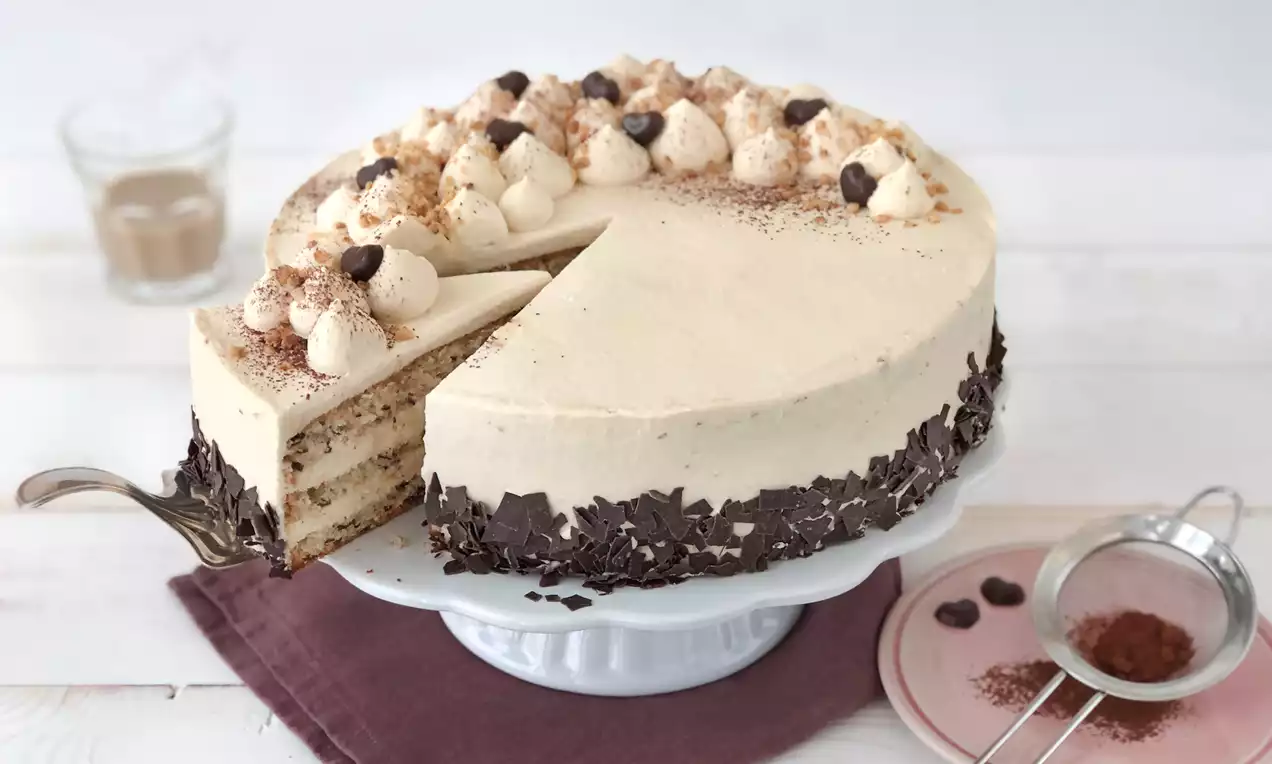 Cremefarbene Baileys-Torte mit Schokotupfen und Kakaopulver, dekoriert mit Schokospänen am Rand auf einer weißen Tortenplatte