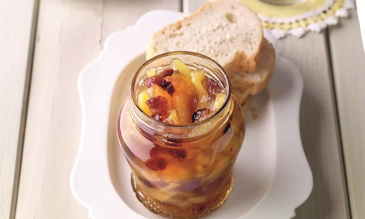 Šareni voćni džem u staklenoj tegli s vidljivim komadićima žutog, crvenog i narančastog voća, serviran na bijelom tanjiru s kriškom hljeba