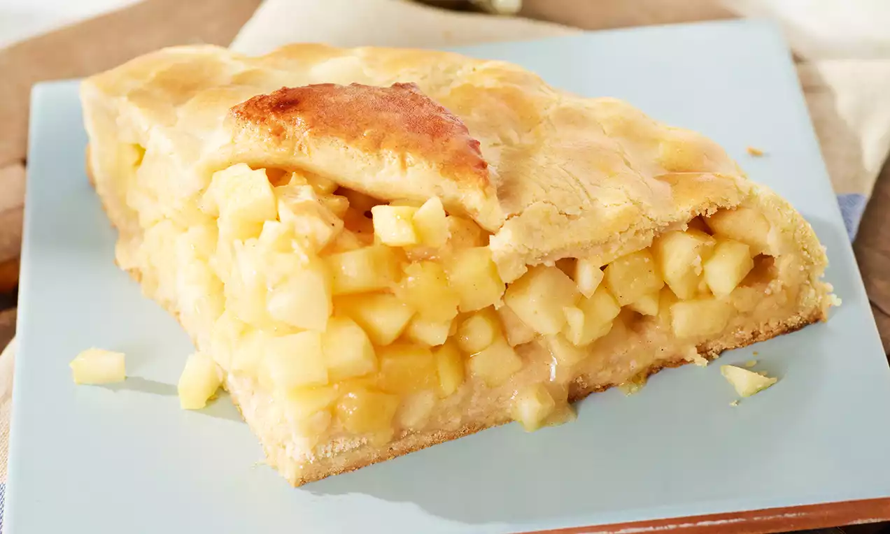 Partie triangulaire de tarte aux pommes dorée, garnie de morceaux de pommes juteux et brillants emprisonnés dans une pâte fine sur une assiette bleue