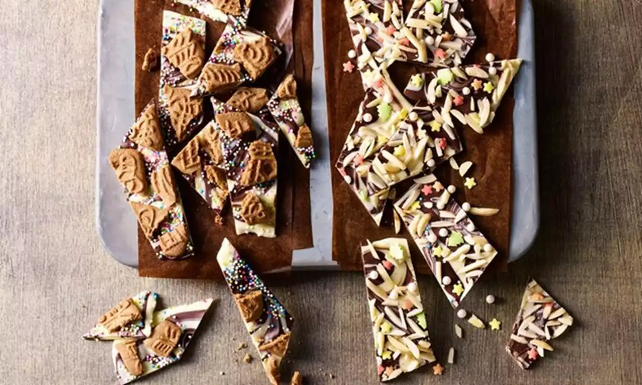 Morceaux irréguliers de chocolat marbré brun et blanc ornés de biscuits bruns, amandes effilées, éclats colorés et étoiles en sucre