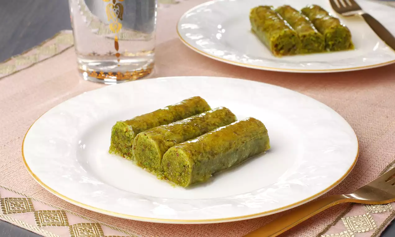 İnce ve altın çizgili porselen tabakta servis edilmiş, parlak şerbetli ve yoğun yeşil püresiyle dolgun Antep fıstıklı sarma
