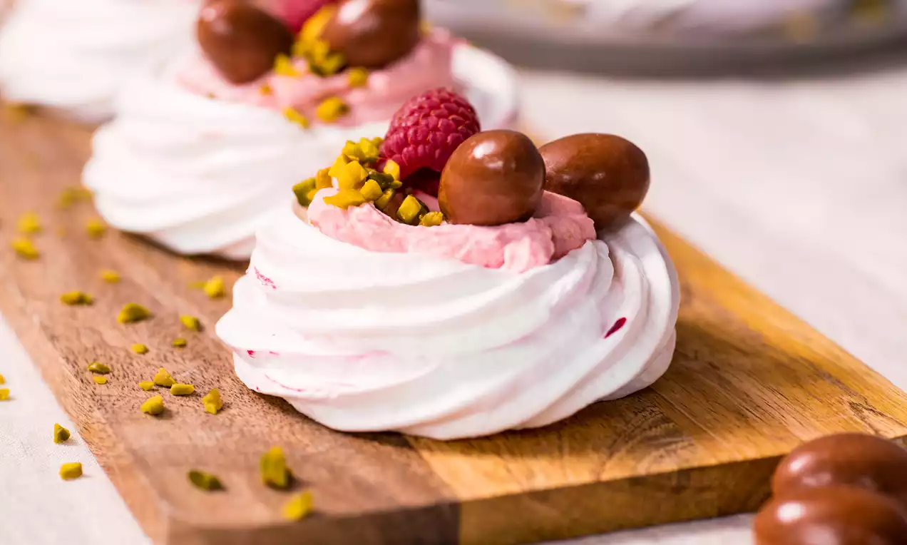 Petites meringues blanches et roses garnies de mousse rose, framboises, oeufs en chocolat et éclats de pistache sur une planche en bois