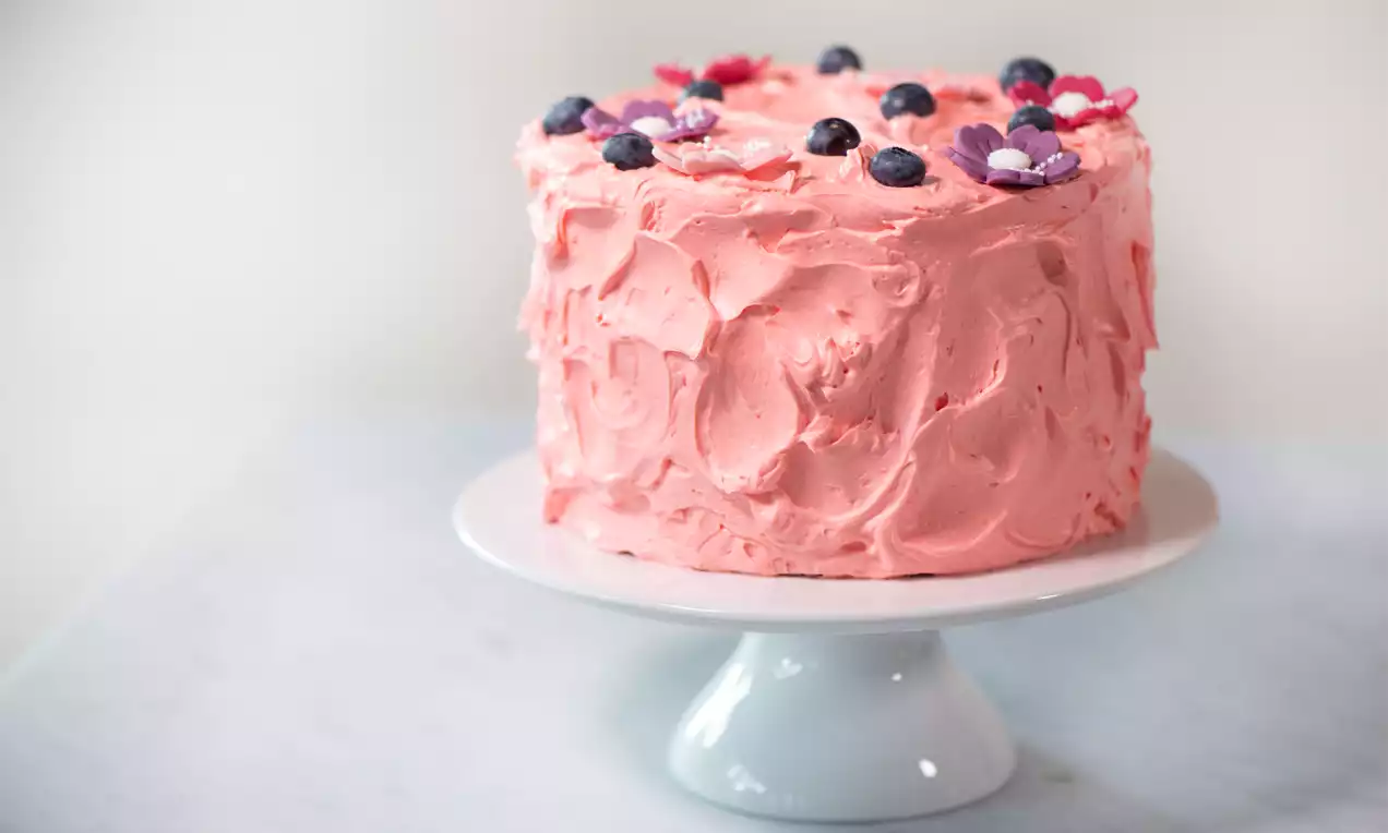 Kleine hohe Torte, wild mit rosa Creme eingestrichen und mit Beeren und Marzipanblüten dekoriert.