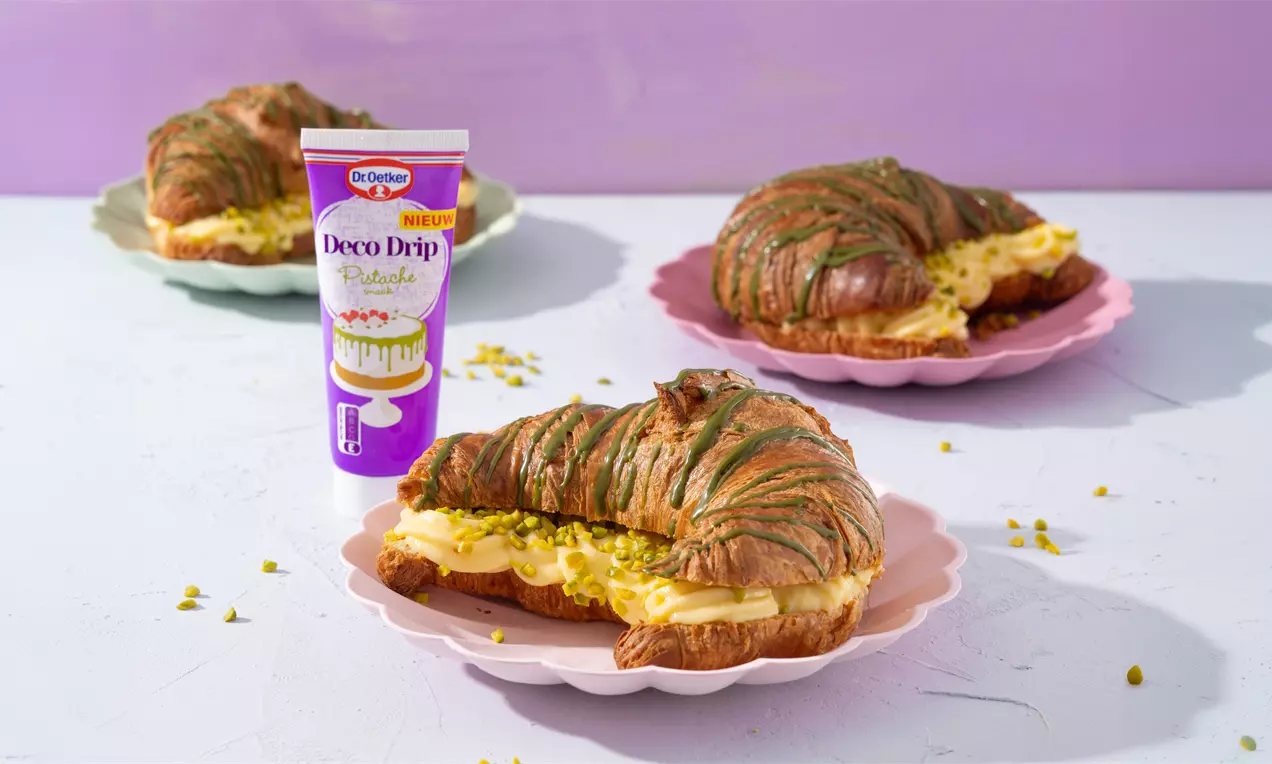 Goudbruine croissants met groene pistachetopping gevuld met gele banketbakkersroom op pastelroze bordjes met een paar pistachekruimels