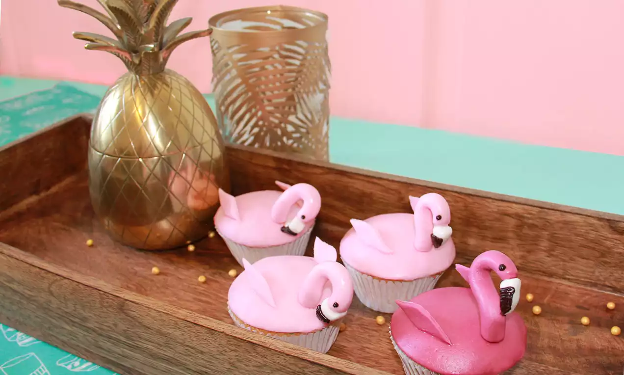 Cupcakes roses décorés de flamants roses en pâte à sucre, disposés dans un plateau en bois avec un ananas doré en arrière-plan