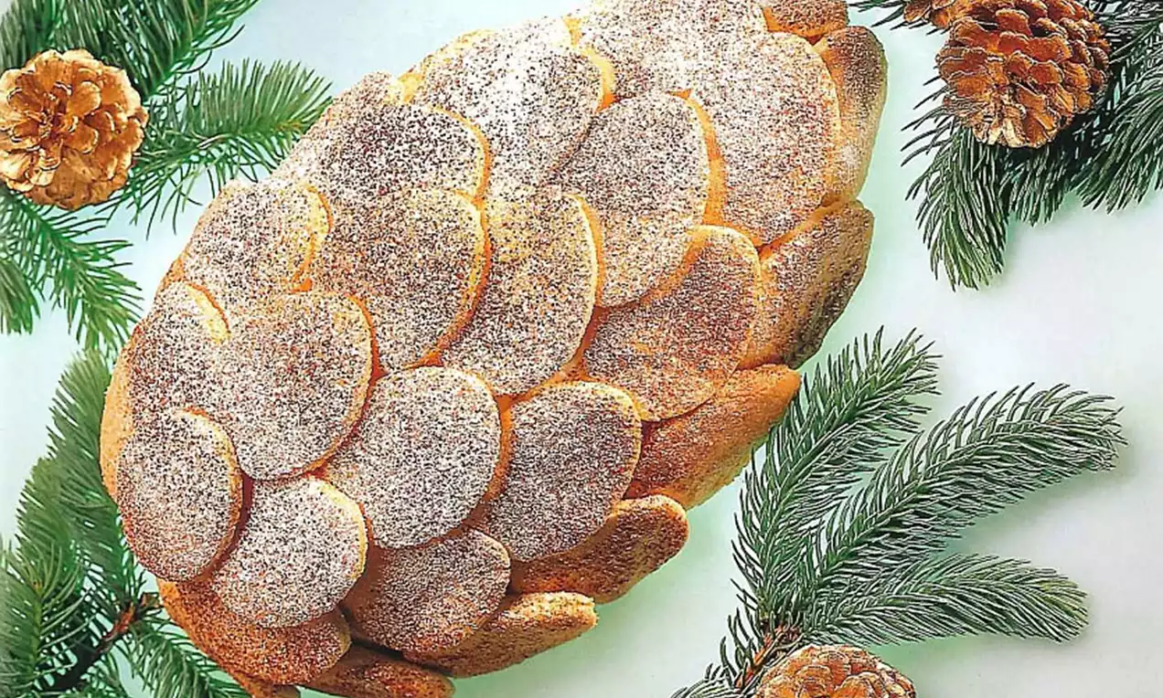 Groot formaat dennenappelcake met goudbruine, poedersuiker bestrooide schaalvormige segmenten, liggend tussen groene dennentakken