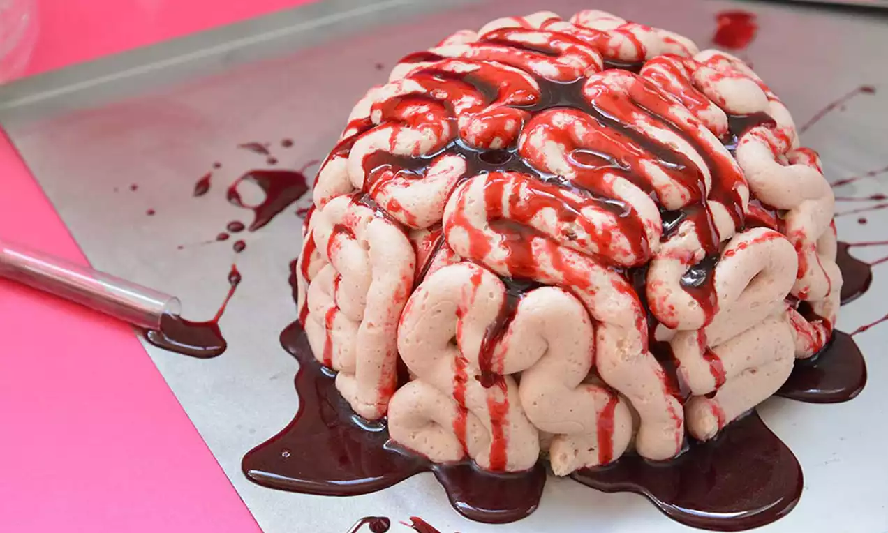 Lyserød hjernekage med glat tekstur og snoede folder dækket med mørkerød sirup på en sølvfarvet bageplade