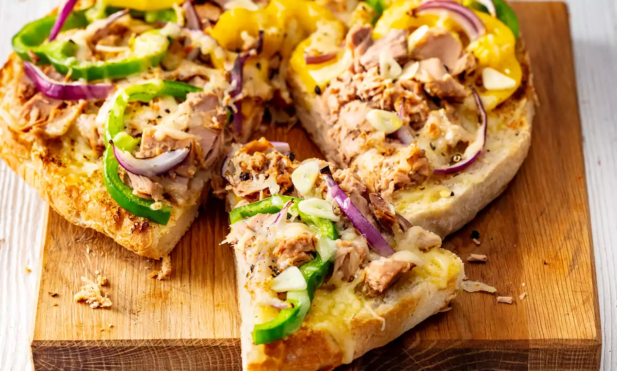Rustikales Pizza-Flatbread mit goldbraunem Boden, belegt mit gelben Paprikastreifen, roten Zwiebeln, grünem Pfeffer und Thunfisch auf Holzbrett