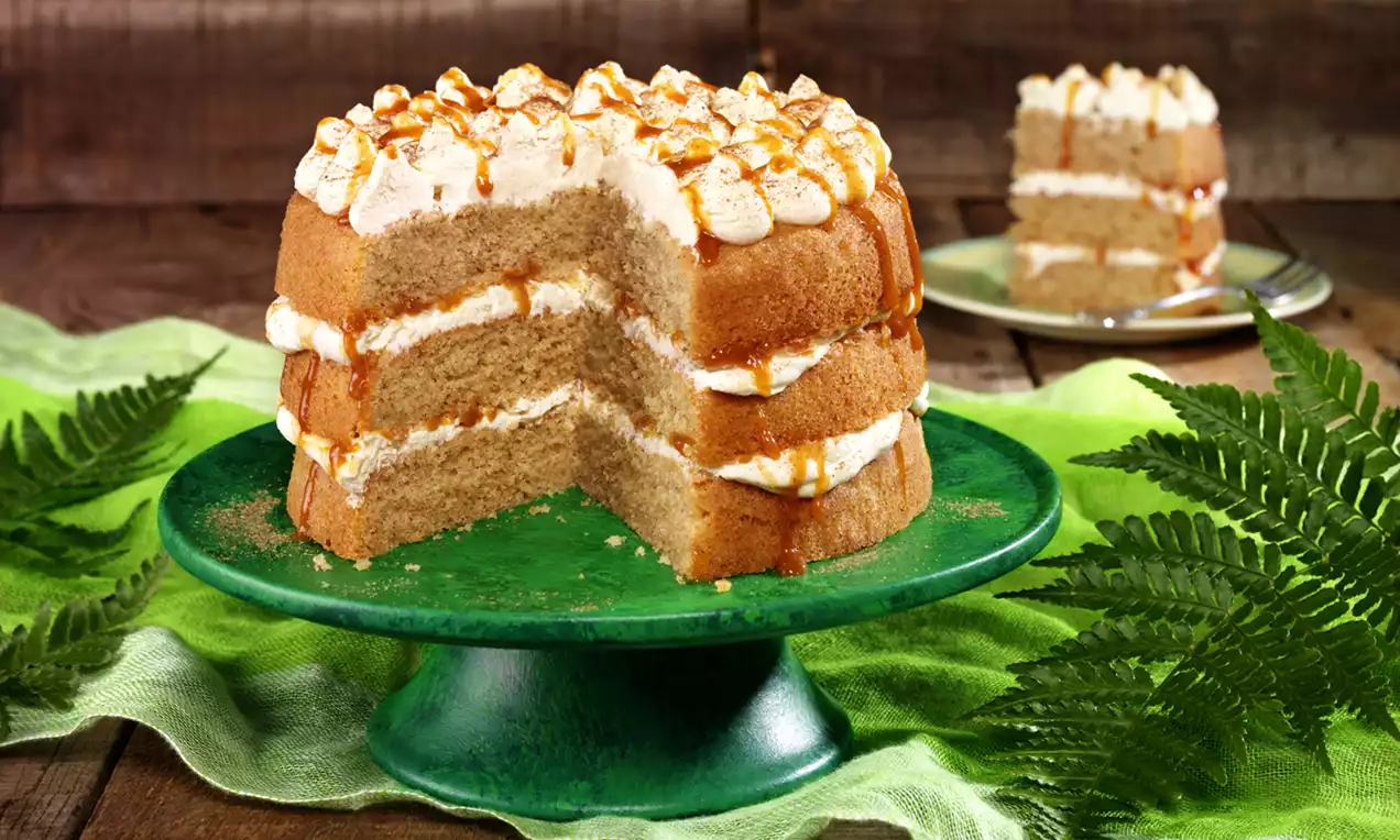 Three-layer caramel and chai spice cake with fluffy cream filling, piped cream swirls, caramel drizzle, and a slice served on a plate