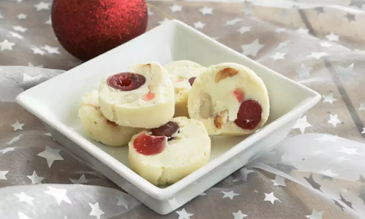 Skiver av hvit konfekt med røde og lilla kirsebær samt nøttebiter anrettet i en firkantet, hvit skål på en stjerneprydet duk