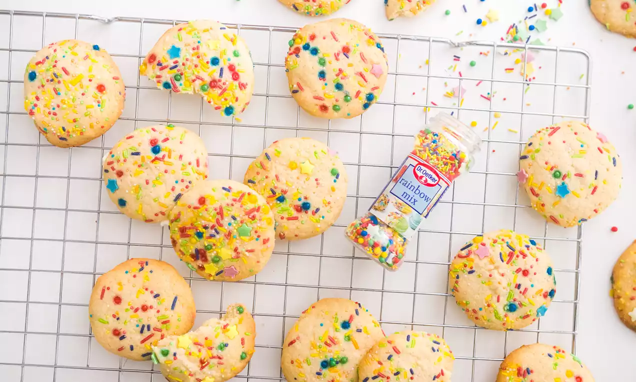 Galletas redondeadas de masa dorada con textura suave salpicadas de sprinkles multicolores dispuestas sobre rejilla metálica