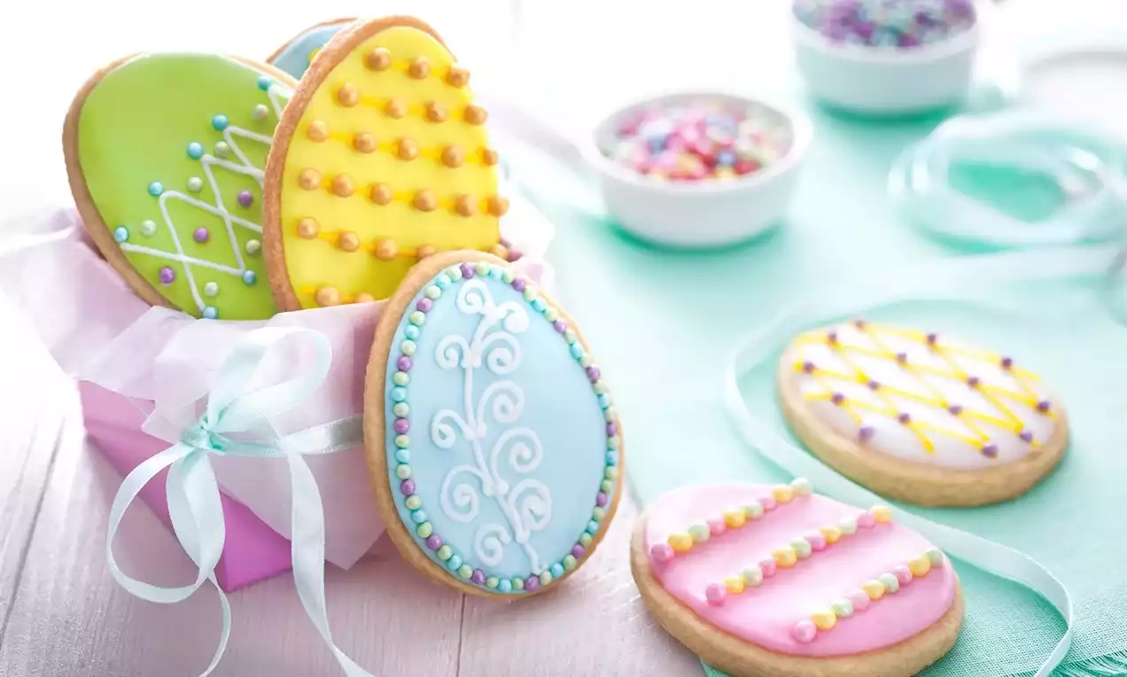 Easter egg-shaped cookies with pastel green, pink, and blue icing, decorative piped patterns, and sprinkles in a pink box tied with ribbon