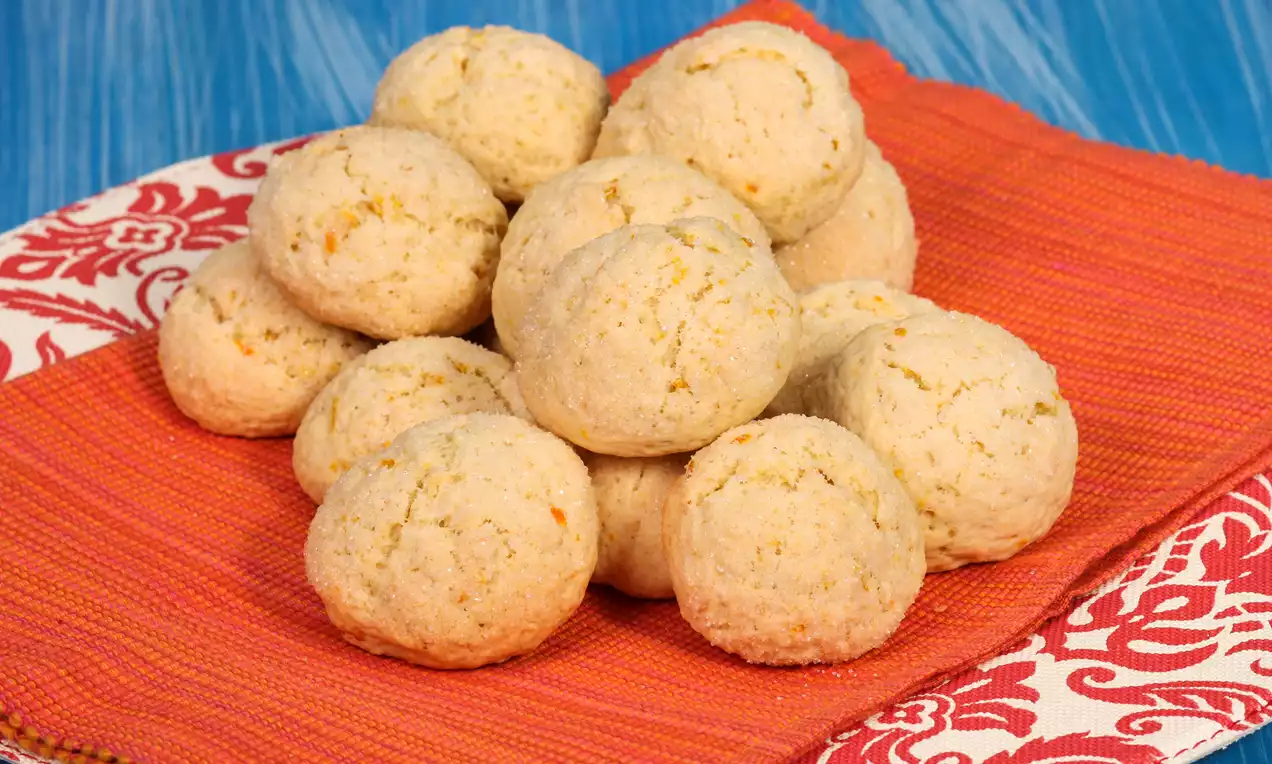 Portakal kabuğu parçacıkları içeren yuvarlak ve çatlak görünümlü kurabiyeler, kırmızı desenli bir örtü üzerinde üst üste yerleştirilmiş