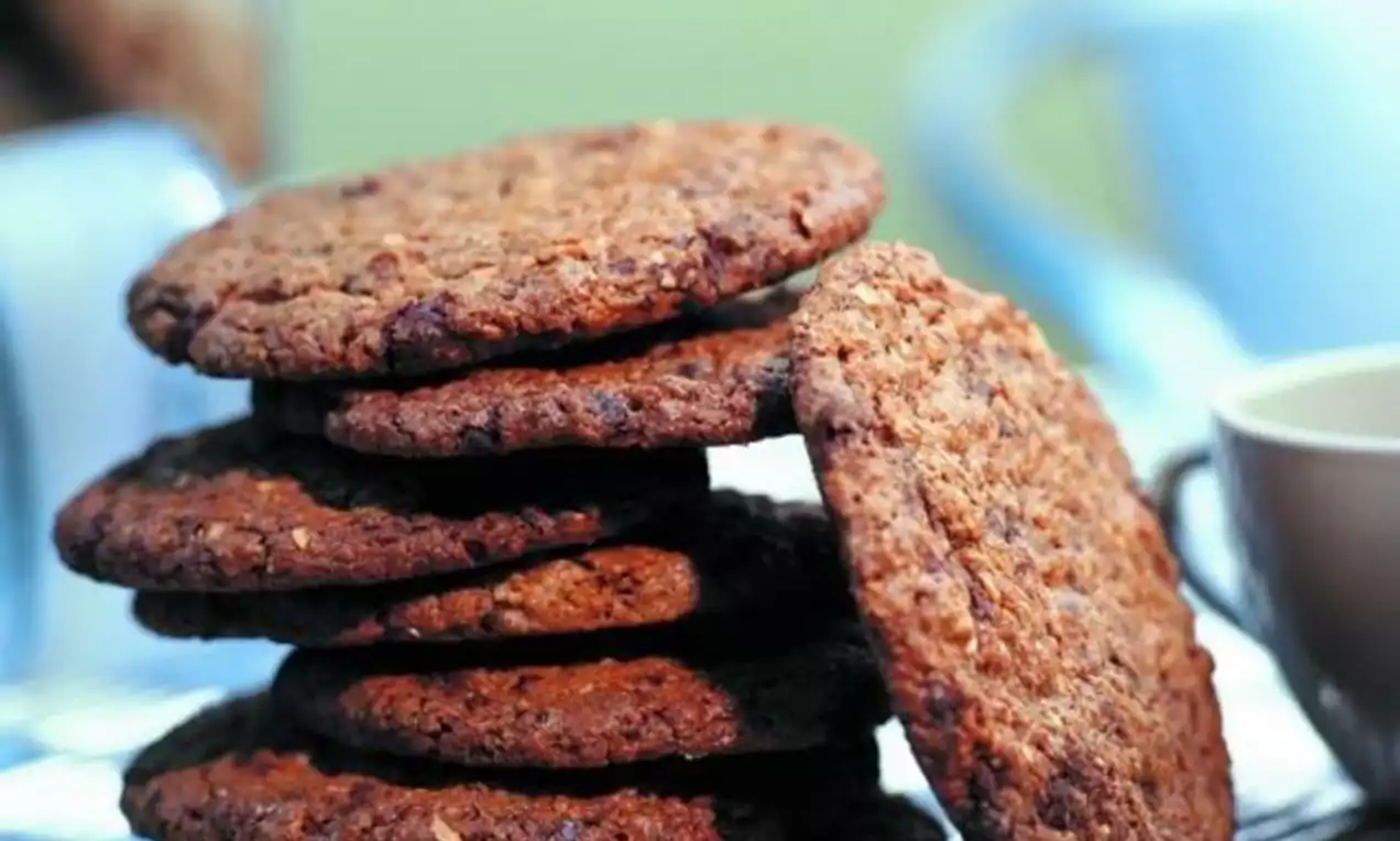 Stablede, gyllenbrune sjokoladecookies med grov tekstur på et sølvfarget fat ved siden av en beige kopp og uskarpt grønt bakgrunn