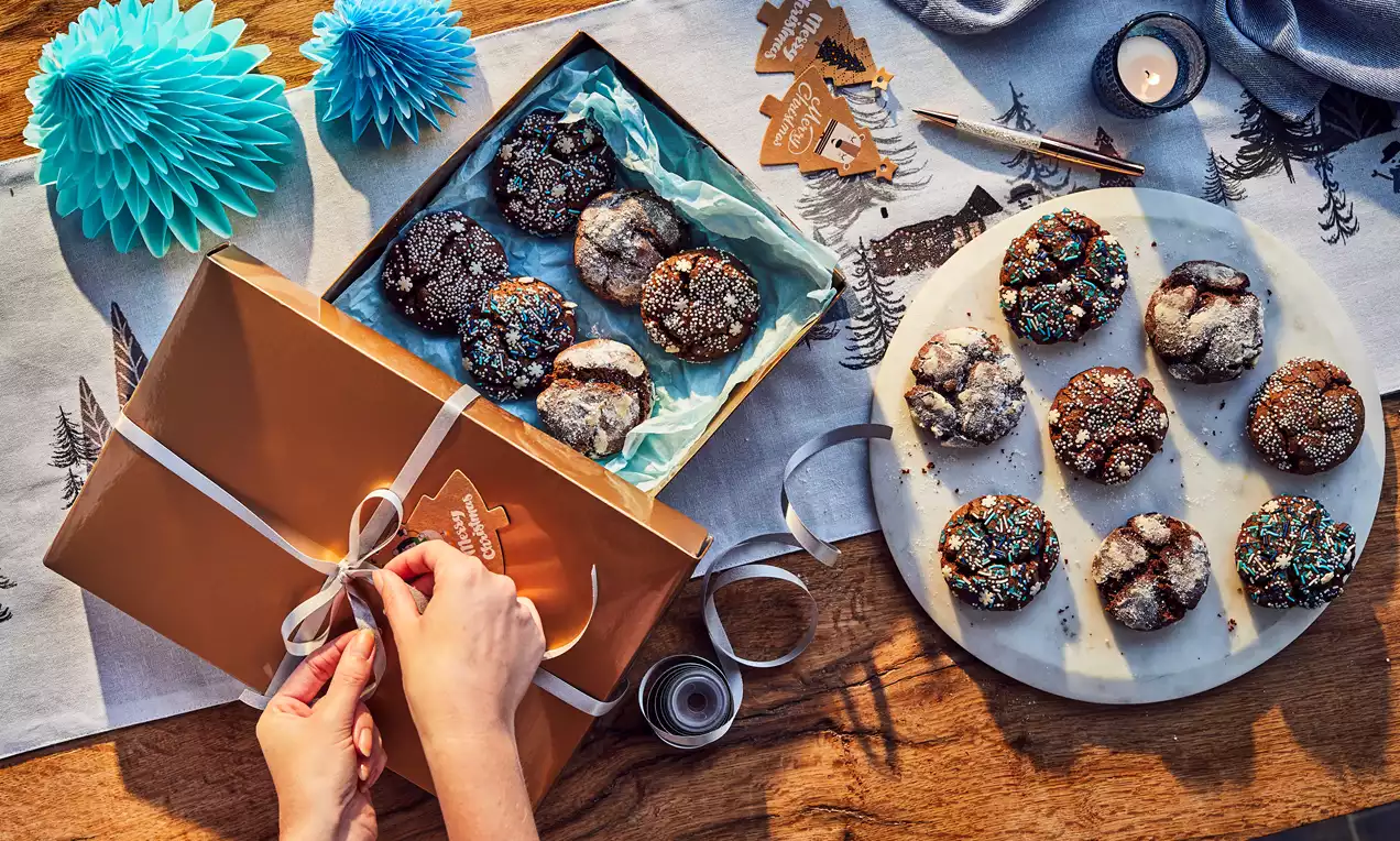 Christmas Crinkle Cookies with crackled powdered sugar tops and festive sprinkles arranged on a round plate and gift box amidst decorations