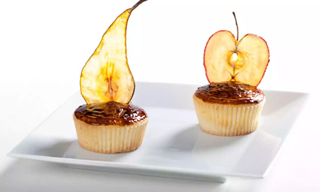 Cupcakes dorés au glaçage brillant, ornés de fines tranches translucides de poire et pomme, présentés sur une assiette blanche carrée