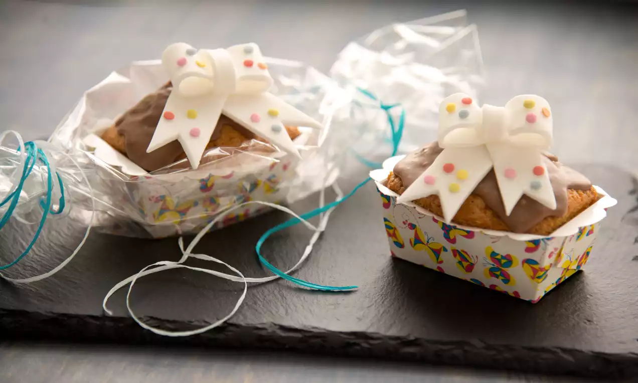 Mini babeczki w kolorowych papilotkach z brązowym lukrem, udekorowane białymi kokardkami z cukrowymi kropeczkami, zapakowane w celofan