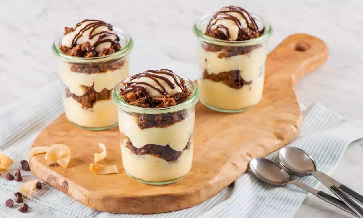Layered chocolate Nanaimo parfaits in clear glass jars with creamy yellow filling, crumbled chocolate layers, and chocolate drizzle on top